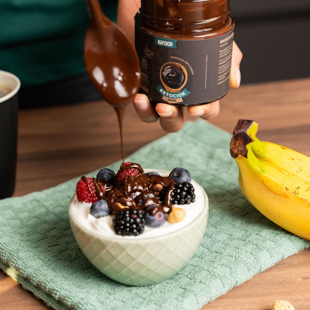 Ketociok Dark versata su una coppetta di yogurt bianco con lamponi, mirtilli e more