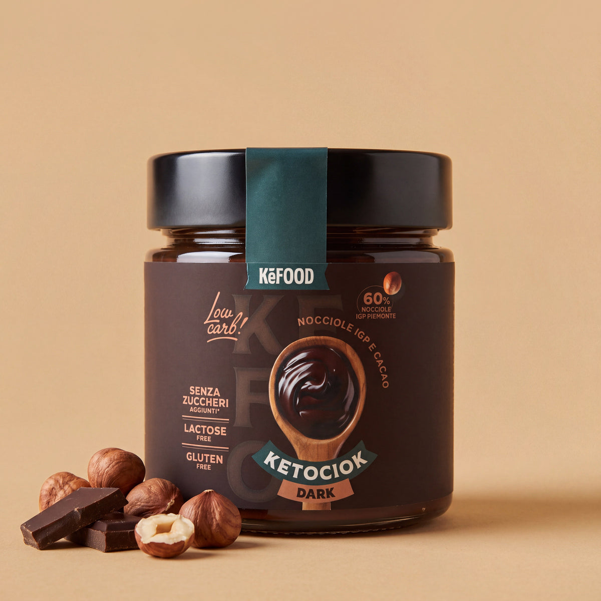 Barattolo di Ketociok Dark Kefood da 250 g, crema spalmabile con 60% nocciole IGP Piemonte e cacao, con nocciole e cioccolato fondente su fondo sabbia