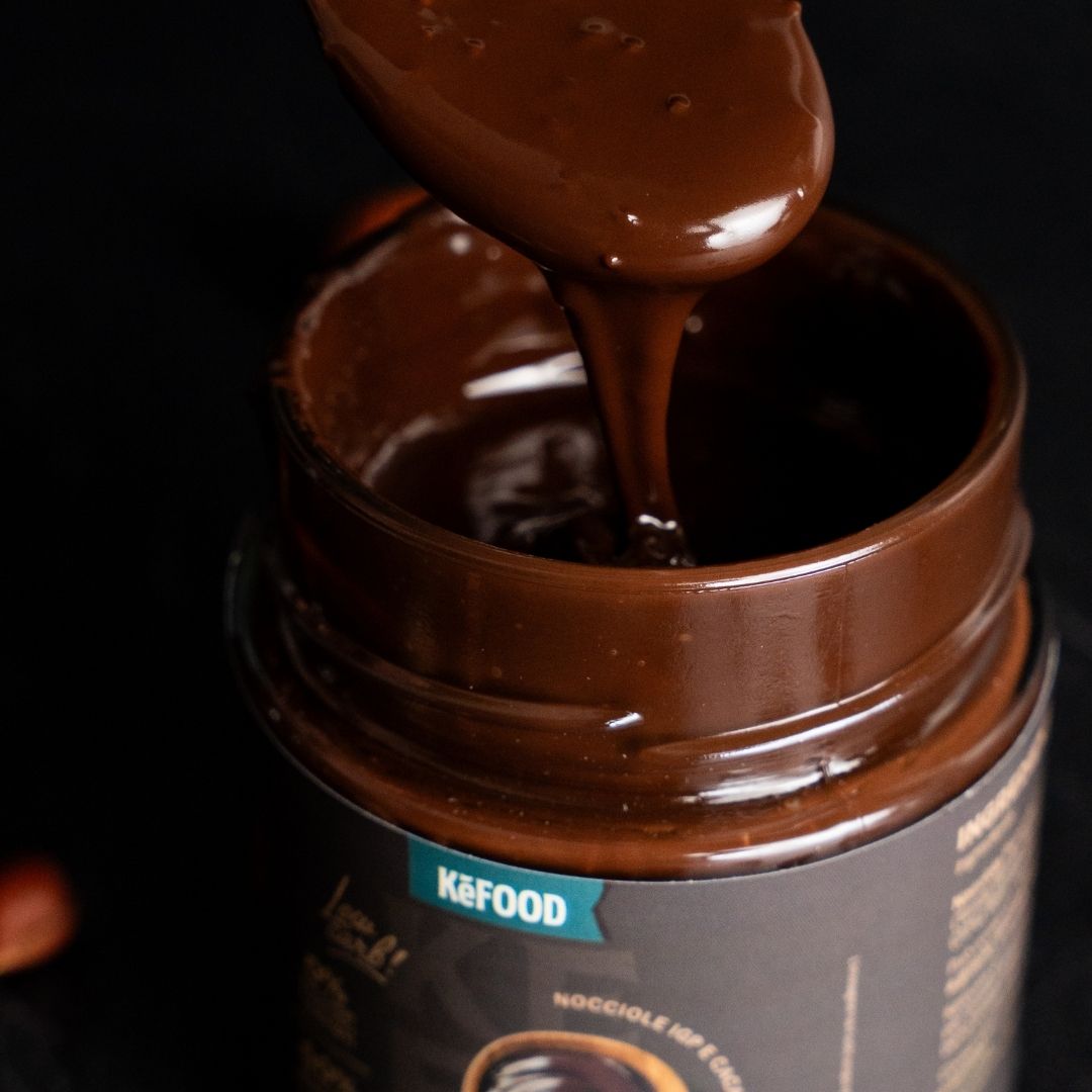 Crema Ketociok Dark densa che cade dal cucchiaio dentro il barattolo aperto